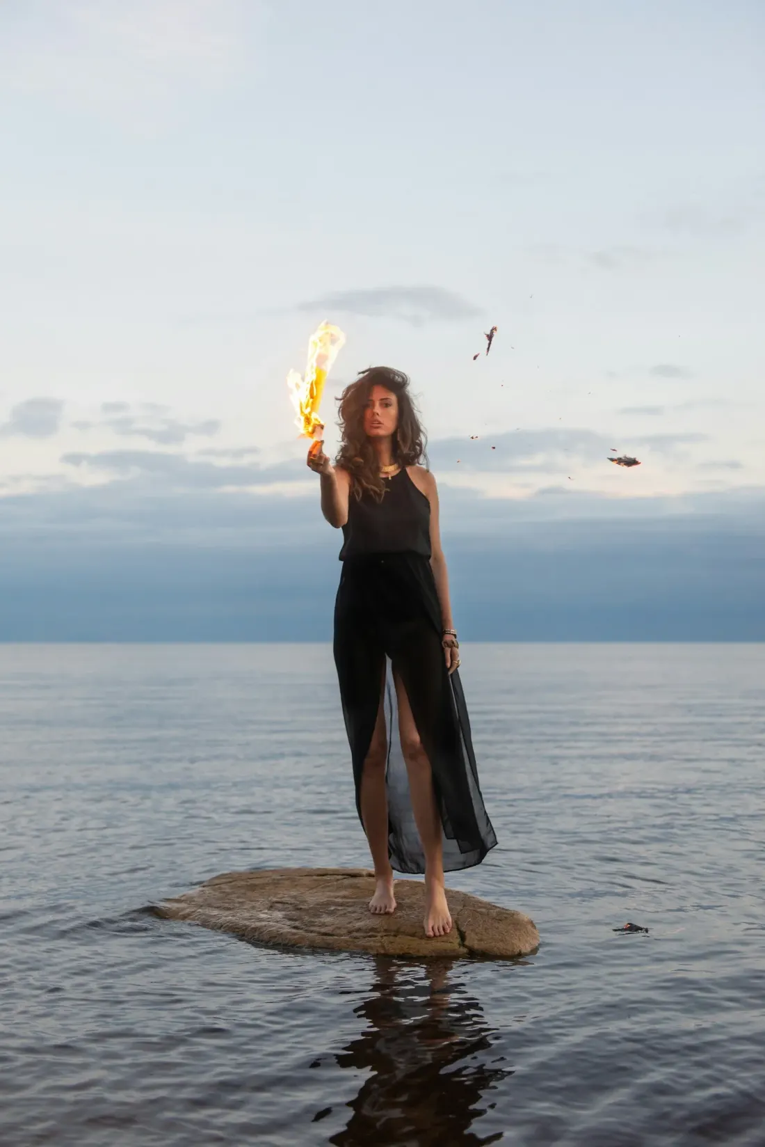 A woman standing in the water holding a flame